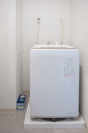 A white appliance, possibly a refrigerator or freezer, with a control panel on the front, placed on a white base. - The Peak Chiyozaki Elite (Chiyozaki, Nishi Ward)