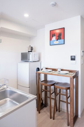 A compact kitchen with a microwave, a kettle, and a small dining table with stools. - The Peak Chiyozaki Elite (Chiyozaki, Nishi Ward)