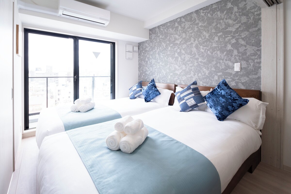 A hotel room with two beds, a large window, and a city view.