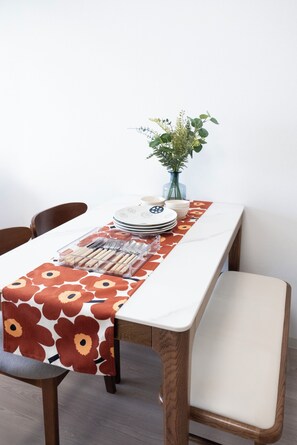 A dining table with a floral tablecloth, a vase with green plants, and a set of plates, forks, and spoons. - The Peak Chiyozaki Elite (Chiyozaki, Nishi Ward)