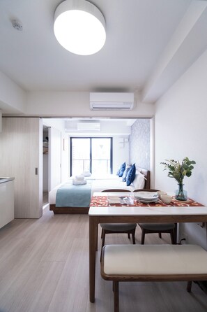 Een moderne hotelkamer met een zithoek, een bed met blauwe kussens, en een vaas met bloemen op de tafel.