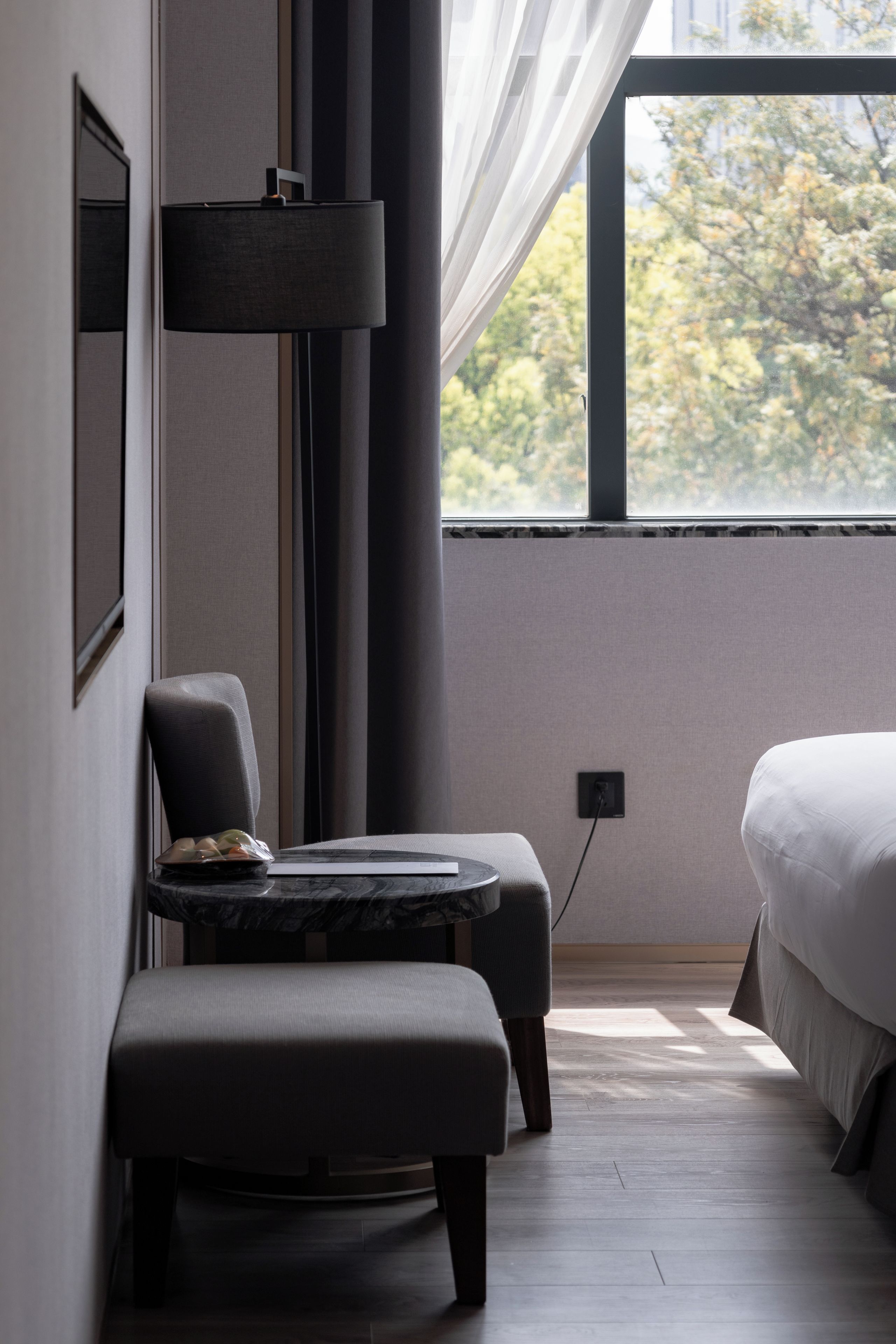 A modern bedroom with a bed, a chair, a small table, and a window with curtains.
