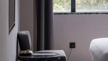 A modern bedroom with a bed, a chair, a small table, and a window with curtains.