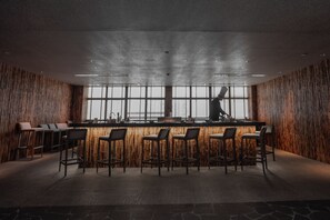 A modern bar area with bamboo wall panels, a bar counter, and multiple bar stools.