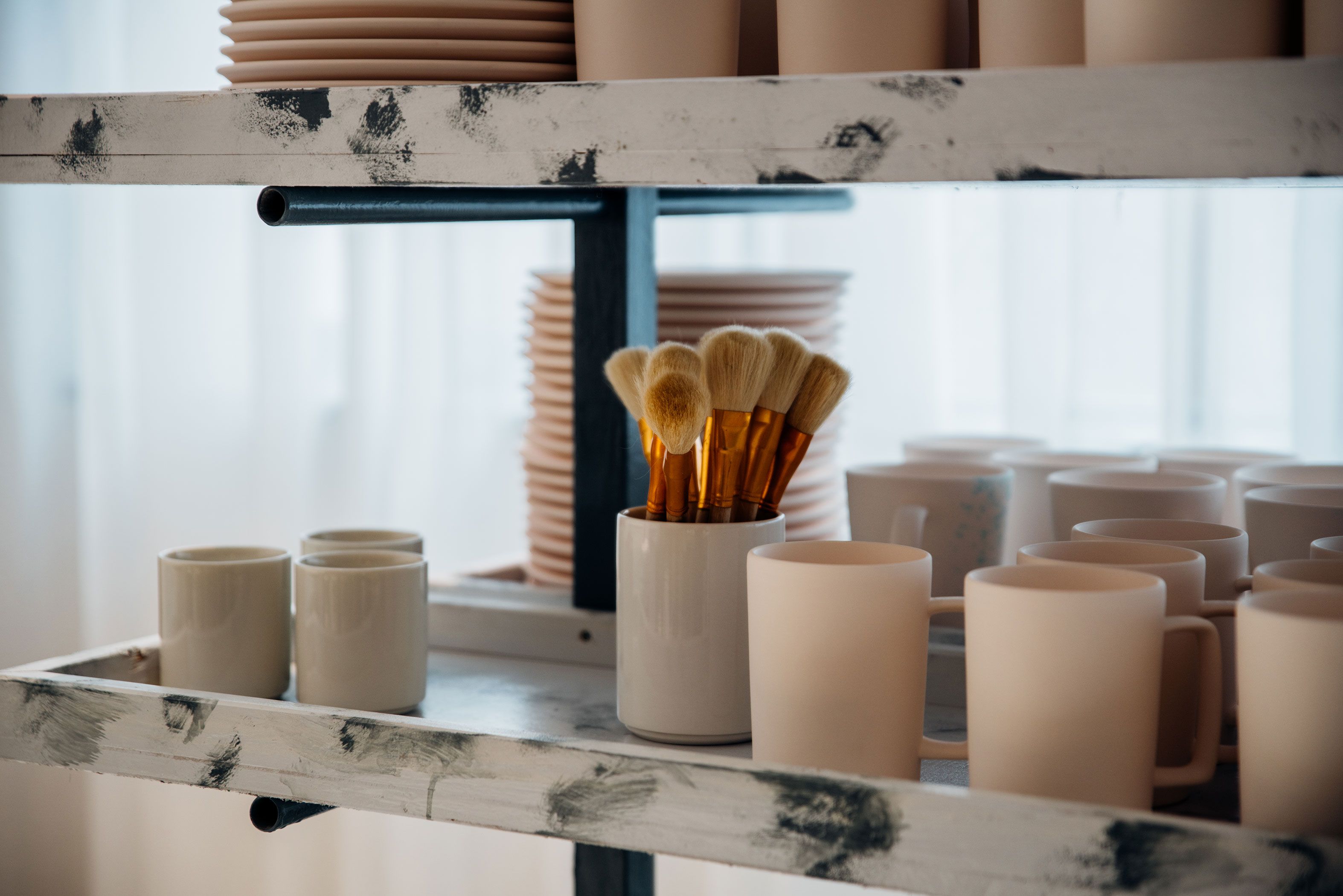 Una estantería con tazas de cerámica, un recipiente con brochas y platos apilados.