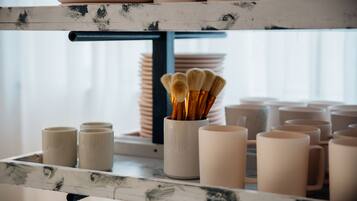 Una estantería con tazas de cerámica, un recipiente con brochas y platos apilados.