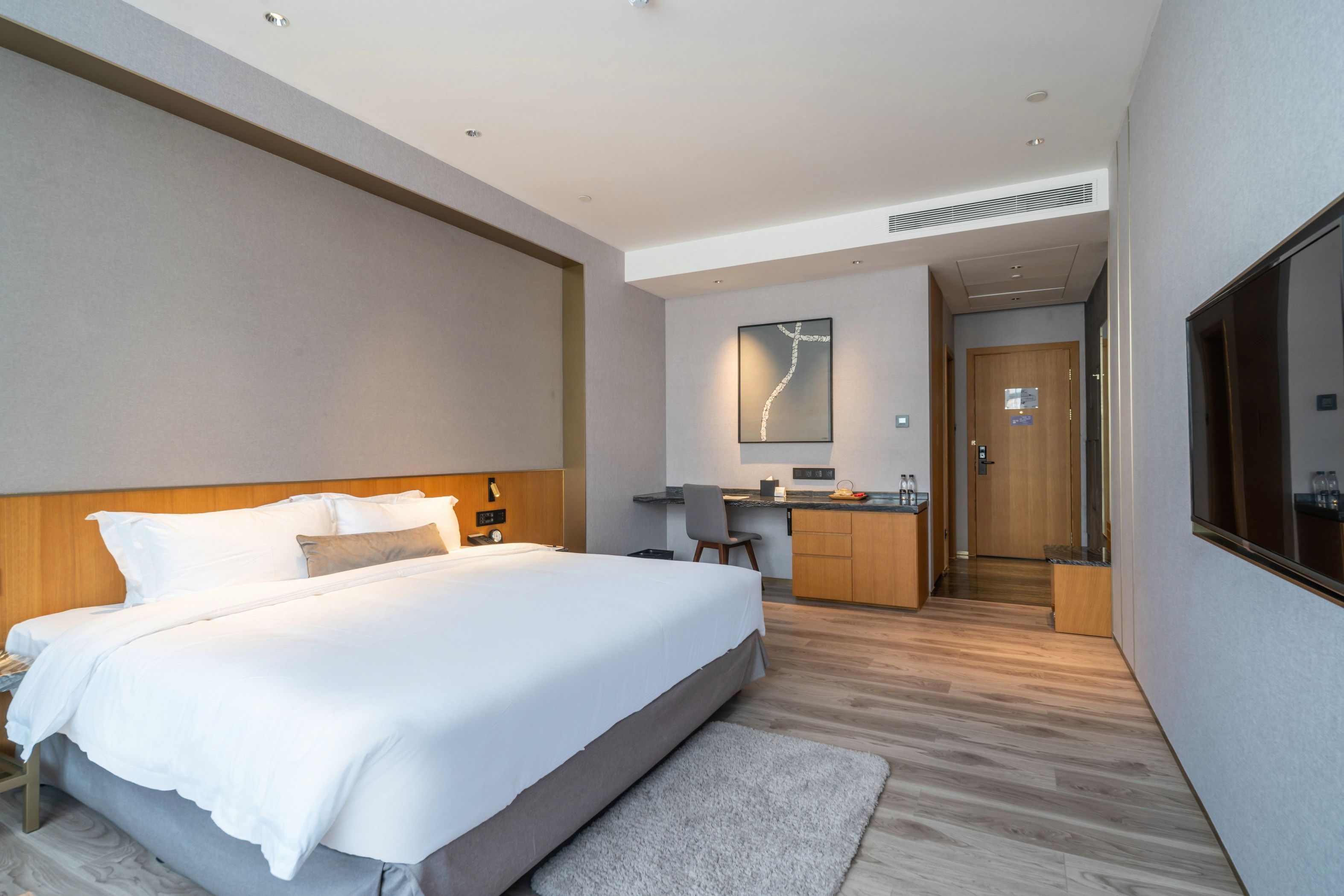 A modern hotel room with a large bed, a desk, and a kitchenette.