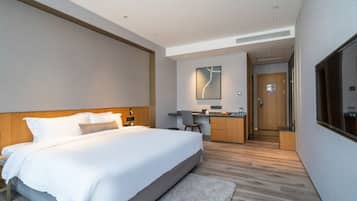 A modern hotel room with a large bed, a desk, and a kitchenette.