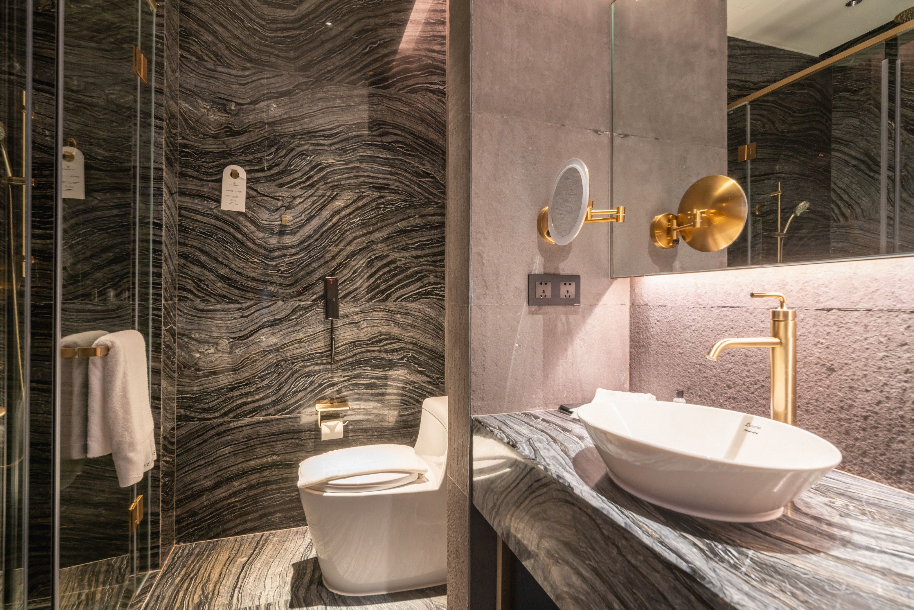 A bathroom with a marble wall, a white sink, and a gold faucet.