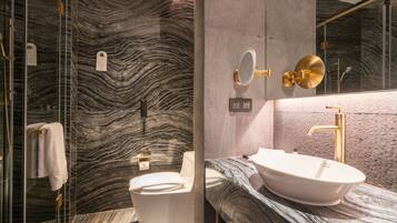 A bathroom with a marble wall, a white sink, and a gold faucet.