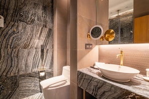A bathroom with a marble wall, a white sink, and a gold faucet.