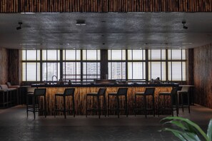 Un bar moderne doté d’un long comptoir, de nombreux tabourets et de grandes fenêtres offrant une vue sur le paysage urbain.