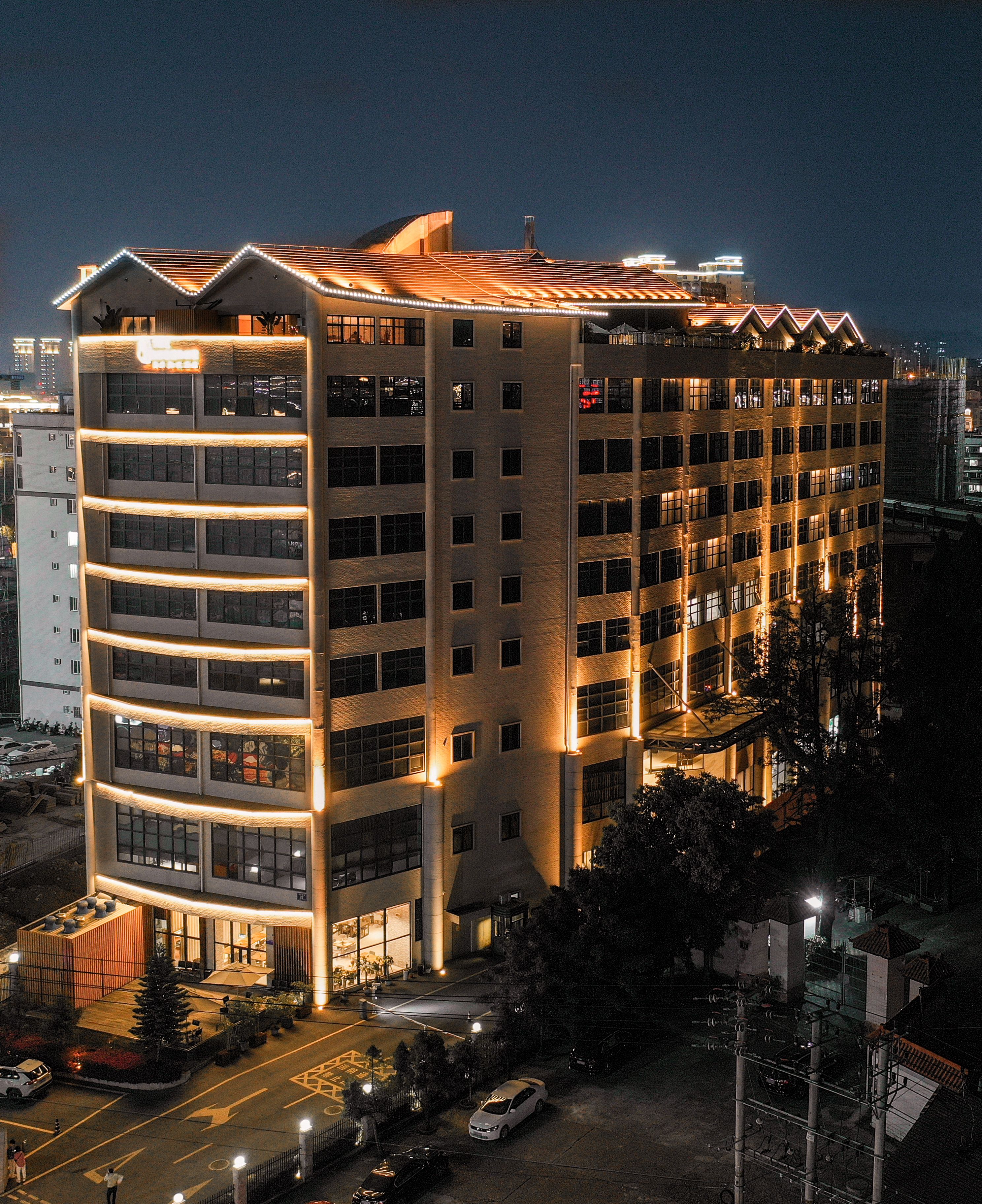 A multi-story hotel with a modern design, featuring balconies and a parking area.