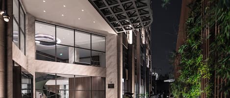 A modern building with a glass facade, a curved entrance, and a covered outdoor area with seating.