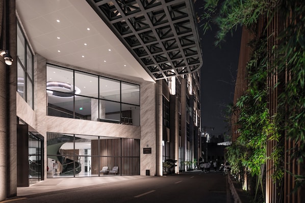 A modern building with a glass facade, a curved entrance, and a covered outdoor area with seating.
