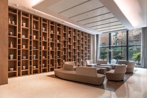 Un intérieur moderne avec un mur entier recouvert d’étagères où sont exposés divers objets en céramique, un coin salon avec des canapés et une grande fenêtre donnant sur un paysage verdoyant.