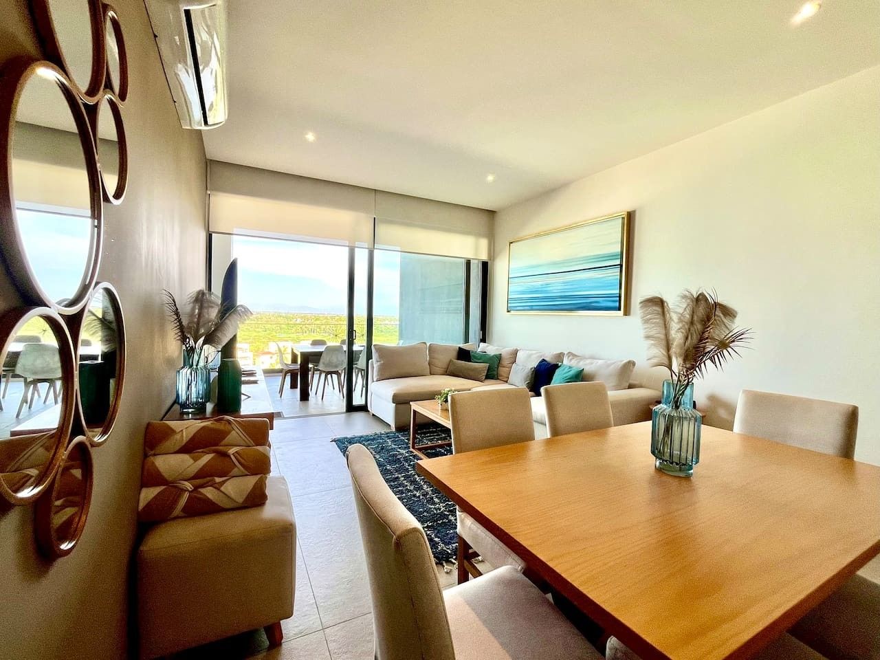 A modern living room with a large wooden dining table, comfortable seating, and a view of the outdoors.