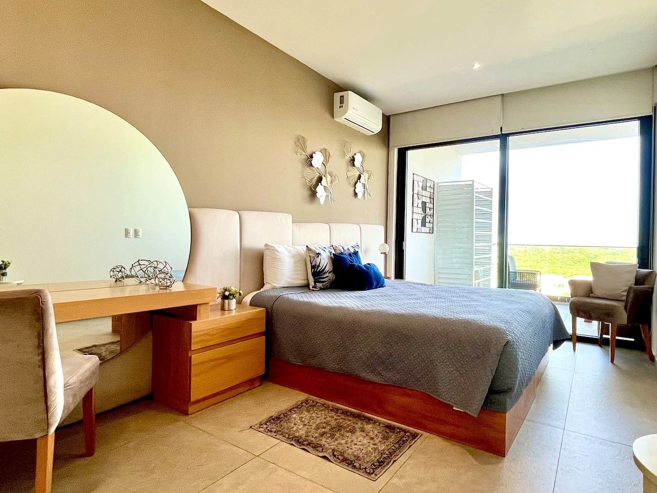 A modern bedroom with a bed, desk, and chair, a large window, and a balcony.