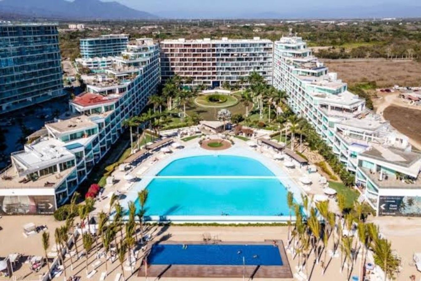 A resort with a central swimming pool, multiple hotel buildings, and a landscaped area with palm trees.