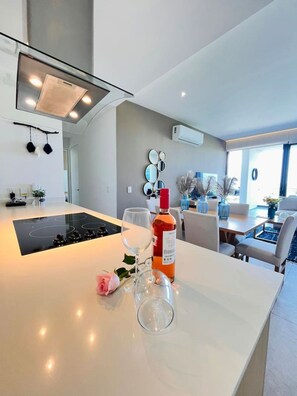 Een moderne keuken met een centraal eiland, een eethoek met tafel en stoelen, en een zithoek met een bank en decoratieve planten.