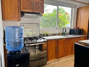 Una cucina con mobili in legno, un piano cottura a gas, un dispenser d'acqua, un forno a microonde e una finestra vista verde.