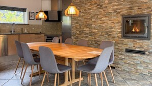 A modern kitchen with a stone wall, a built-in fireplace, and a dining area with a wooden table and chairs. - Cozy home in Kolind with private swimming pool, can be inside or outside (Kolind)