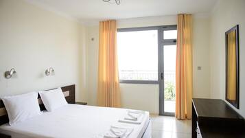 Una habitación de hotel con cama, televisión, escritorio y balcón con cortinas.
