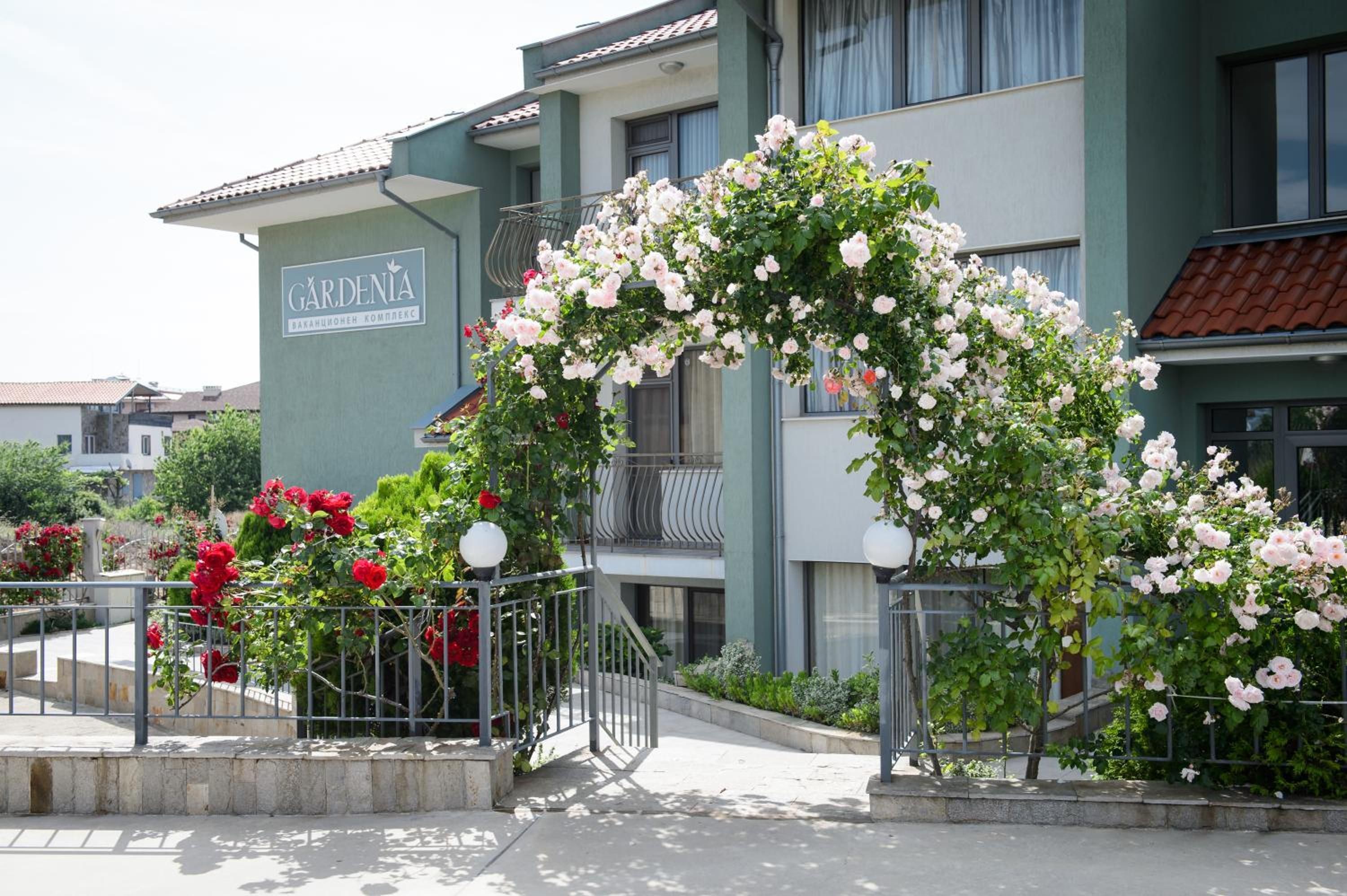 Un edificio con un letrero que dice 'GARDENIA' y un arco decorativo de rosas trepadoras.