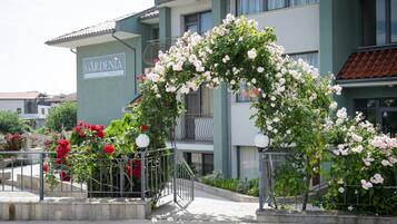 Un edificio con un letrero que dice 'GARDENIA' y un arco decorativo de rosas trepadoras.