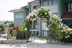 Un edificio con un letrero que dice 'GARDENIA' y un arco decorativo de rosas trepadoras.