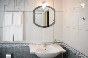 Un baño con un lavabo blanco, un espejo y un perchero con dos toallas blancas.