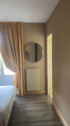 A hotel room with a bed, a radiator, a round mirror, and a door.