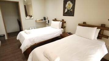 A hotel room with two beds, a bedside table, a mirror, and a wall-mounted flower painting.