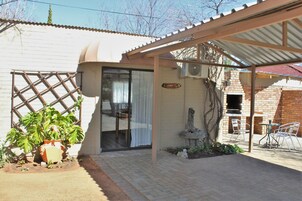 A covered patio area with a brick oven, a pergola, and a seating area with chairs.