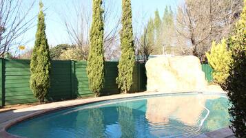 A swimming pool with a stone wall and a green fence.