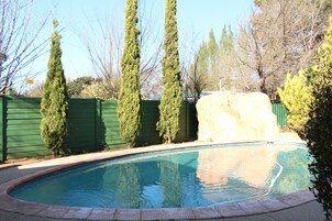 A swimming pool with a stone wall and a green fence.