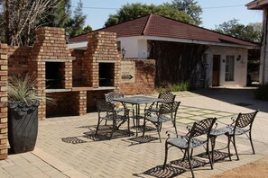 A brick building with a red-tiled roof, a brick barbecue area, and outdoor seating with metal chairs and tables. - The Resting Place Guesthouse (Bloemfontein)
