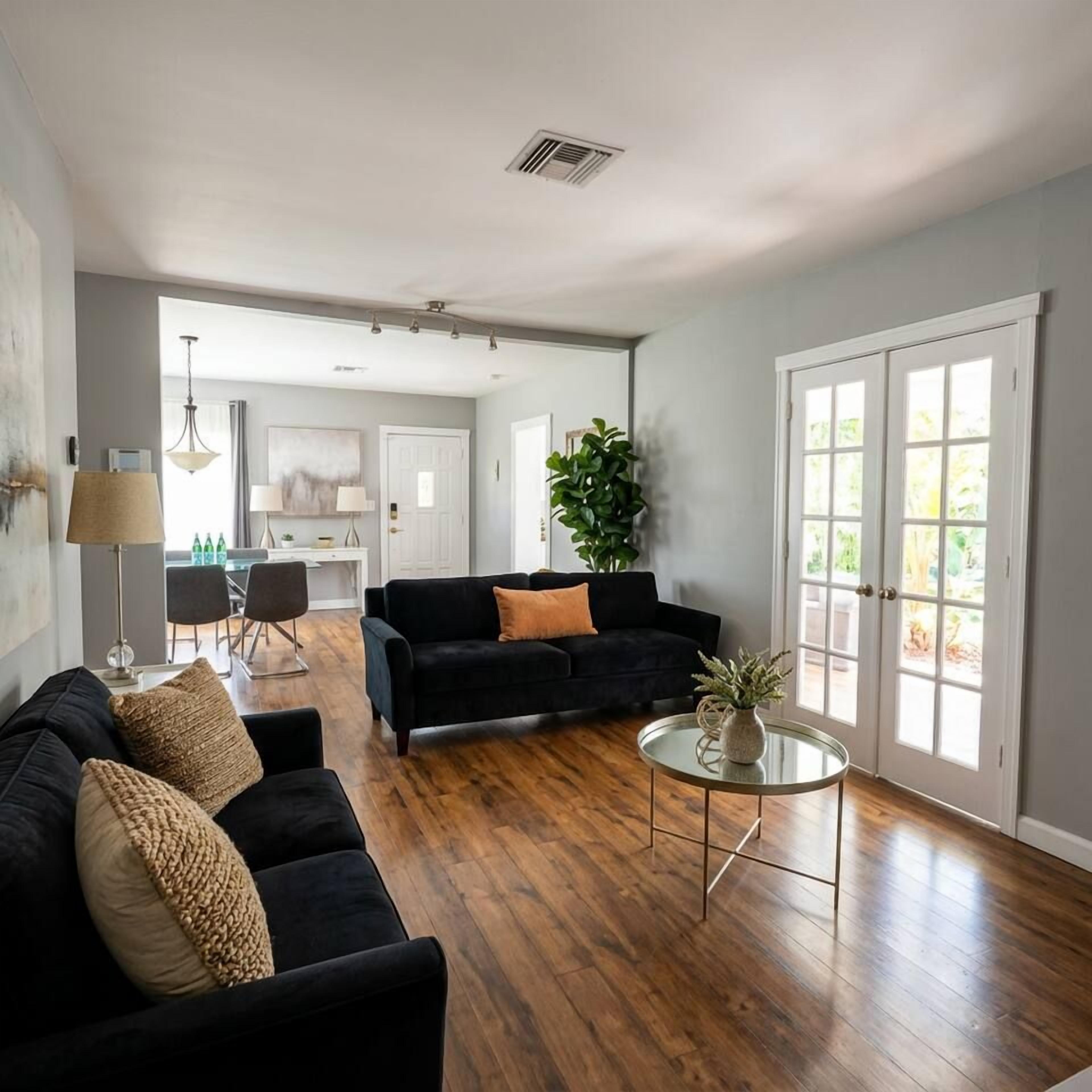 A spacious living room with a dark sofa, a round coffee table, and a dining area in the background.