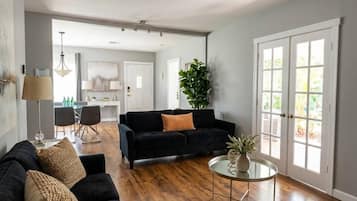 A spacious living room with a dark sofa, a round coffee table, and a dining area in the background.