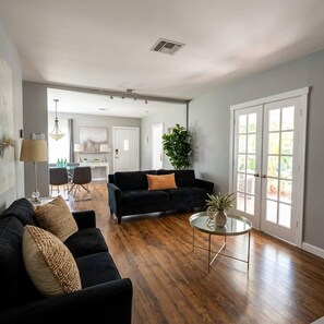 A spacious living room with a dark sofa, a round coffee table, and a dining area in the background.