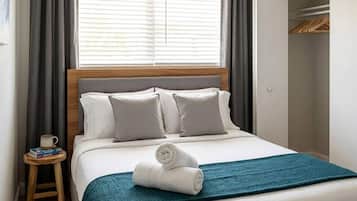 A hotel room with a bed, a bedside table with a mug and books, a ceiling fan, and a wardrobe.