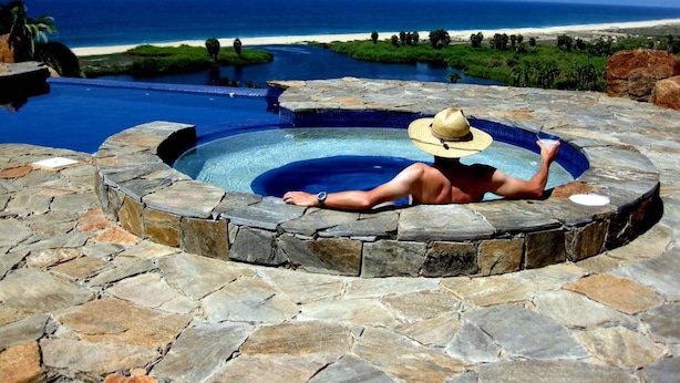 A stone hot tub with a person relaxing, overlooking a beach and ocean. - Las Casitas (Todos Santos)