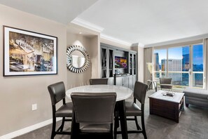Une chambre d’hôtel moderne dotée d’un coin repas, d’une grande fenêtre offrant une vue sur la ville, d’un tableau encadré représentant Las Vegas et d’un miroir rond original.