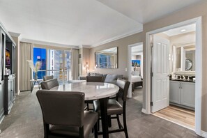 Ett hotellrum med en matplats, en soffa, ett stort fönster med gardiner, en spegel och utsikt över stadsbilden.