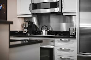 A modern kitchen with stainless steel appliances, including a microwave, coffee maker, kettle, and toaster. - Strip View Suite|On LV Strip w/Balcony/LazyRiver (Las Vegas)