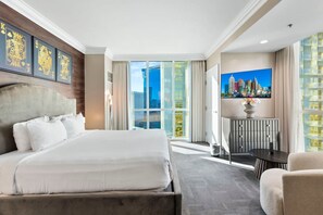 Ett hotellrum med en stor säng, ett skrivbord, en stol och utsikt över staden.