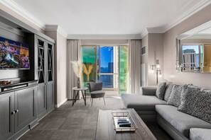 A modern living room with a sofa, a coffee table, a TV, and a view of the city through large windows. - Strip View Suite|On LV Strip w/Balcony/LazyRiver (Las Vegas)