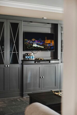 A living room with a flat-screen TV mounted on a grey cabinet, a coffee table in the foreground, and a carpeted floor. - Strip View Suite|On LV Strip w/Balcony/LazyRiver (Las Vegas)
