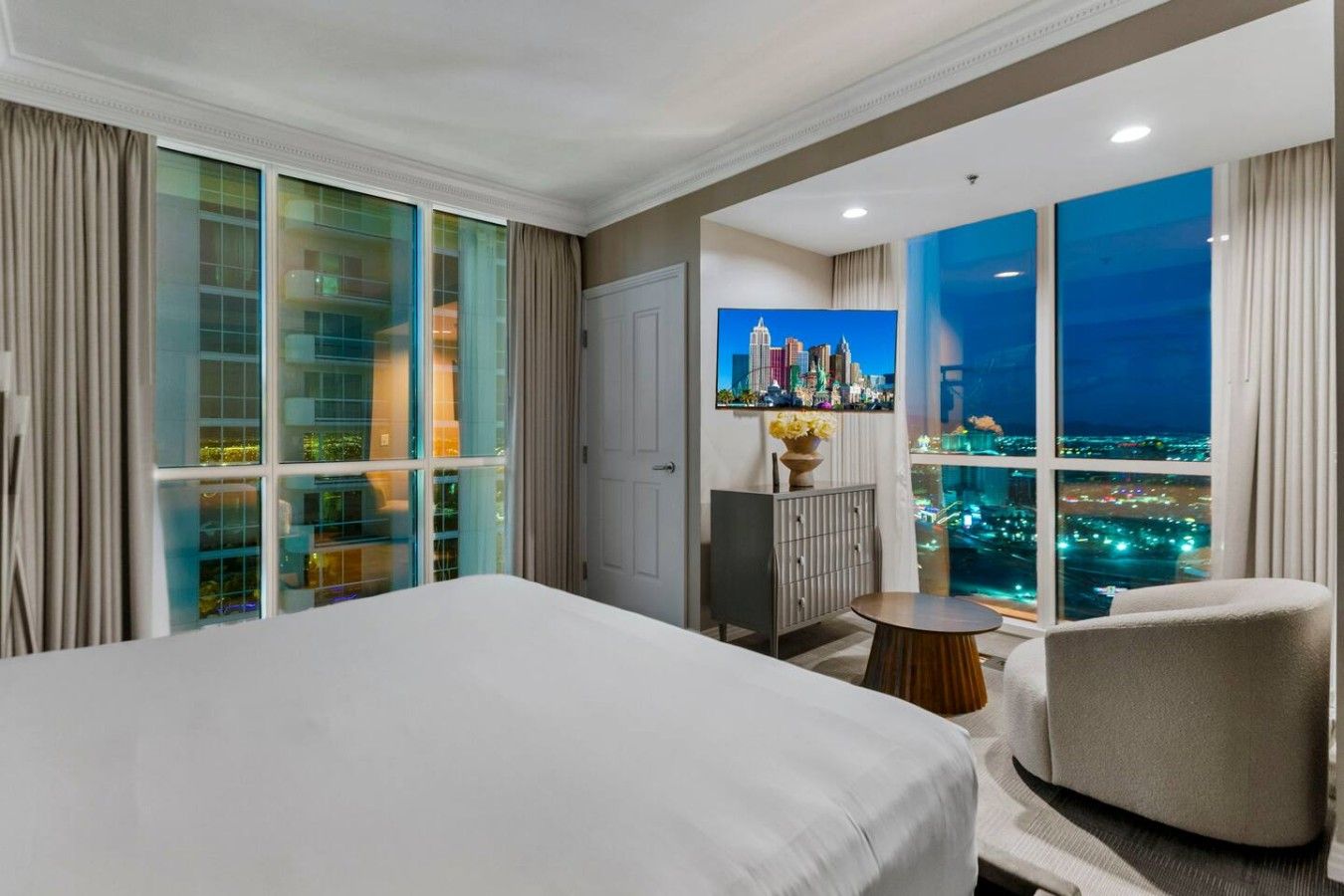 Habitación de hotel con cama, zona de estar, armario y un amplio ventanal con vistas a la ciudad.