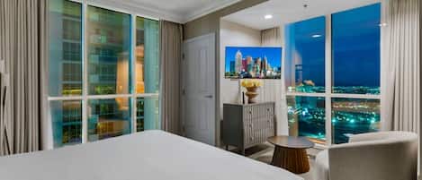 Habitación de hotel con cama, zona de estar, armario y un amplio ventanal con vistas a la ciudad.
